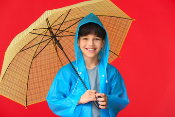 Cute little boy in raincoat and with umbrella on color background