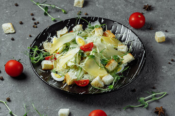Fresh Caesar salad in a black plate on a gray background.Top view