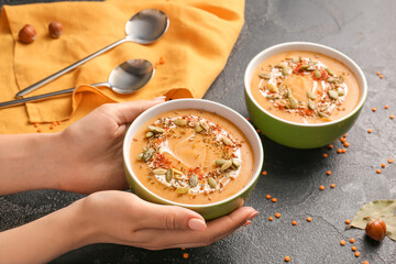 Female hands with tasty lentils soup in bowl on dark background