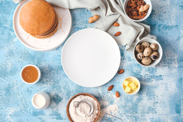 Tasty pancakes with ingredients and plate on color background