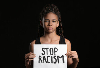 Sad African-American girl with poster on dark background. Stop racism