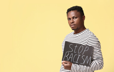 Sad African-American man with poster on color background. Stop racism