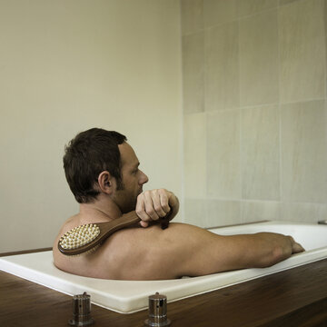 A Man Scrubbing His Back In The Bathtub