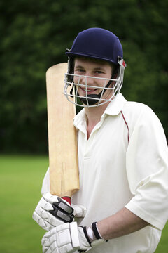 Teenage boy with sports helmet and cricket bat posing for the camera