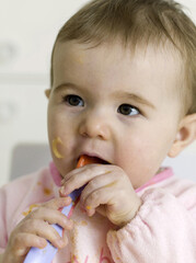 Baby girl with food on face biting on a plastic spoon