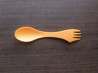 Orange color small plastic backpacking spoon with fork and knife combo kept on wooden table