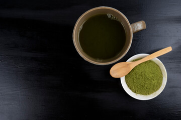 matcha tea brewed in a brown bowl and matcha powder on the side