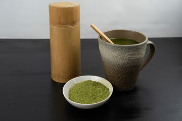 matcha tea brewed in a brown bowl and matcha powder on the side