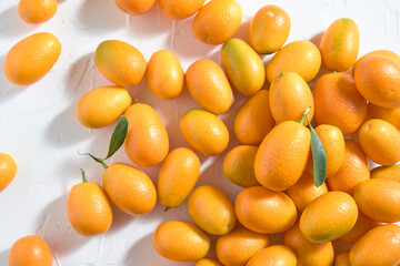 Fresh kumquats, small exotic citrus fruits, on a white textured background