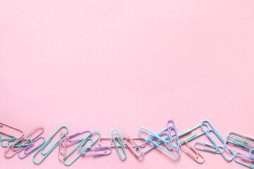 Back to school. Gentle color paper clips laid out on a delicate pink background in a row from the bottom. Layout and flat lay with place for text.