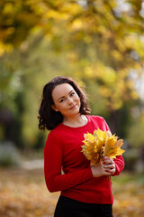 Autumn mood. Romantic Black-haired woman weared in red sweater smiles and walks in a park with beautifull autumn leaves in her hands. Fall coming. Autumn story. Yellow leaves in park