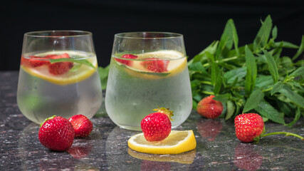 Two glasses of cold water with berries and lemon on a stone background.