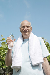 Senior man with towel around his neck holding bottled water