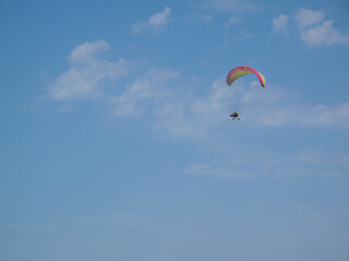 A paraglider flies in the sky under a multi-colored paraglider.