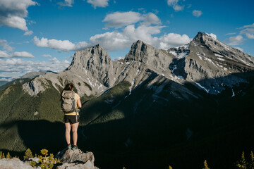 Hiker woman overlooking beautiful mountain scenery of the iconic Three Sisters above Canmore from the summit of Grassi Knob hike, Alberta, Canada