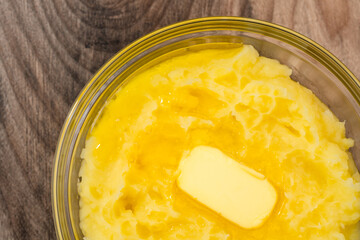 Mushed potato with melting butter close up in a glass bowl on wooden background