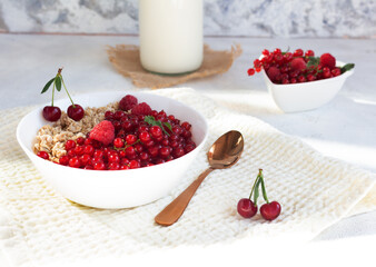 Tasty and healthy breakfast made of granola with berries of red currant, raspberry and cherry with milk in a white bowl. Fitness breakfast on a white background