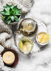 Green tea with lemon, knitted blanket, candle on a white carpet on the floor. Concept of  cozy scandinavian home