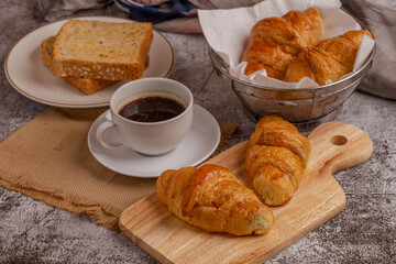 freshly baked croissants and whole wheat bread with black coffee on grey table for breakfast