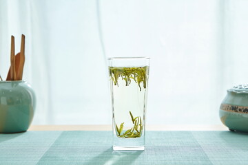 The green table mat with a cup of Mao Feng tea in front of the windowsill, the sun shines on it.