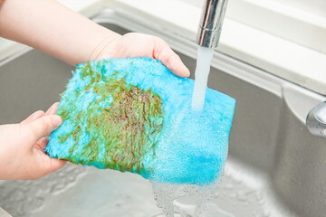 A hand in front of the sink holding a blue cleaning cloth and cleaning the stains on it.