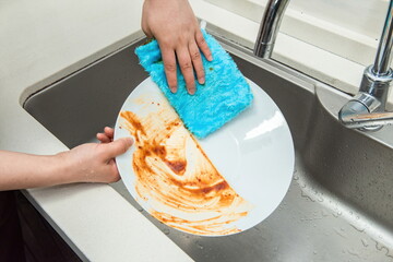 One hand is holding a blue cleaning cloth and washing dishes.