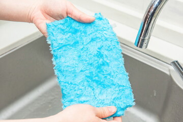 One hand holding a blue dishcloth next to the sink.
