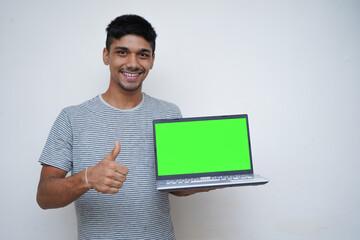 Young handsome asian teen boy showing thumbs up with a laptop on the other hand with a green screen.