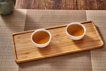 Small white porcelain teacups with ancient black tea in a wooden tray.