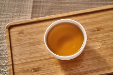 Small white porcelain teacups with ancient black tea in a wooden tray.