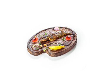 Delicious cooked grilled fish served with a slice of lemon and spices on a wooden board. Decorated with fresh flowers. Healthy, cuisine. Isolated.