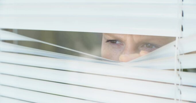 Curious woman looking out through Venetian window blinds, close up shot.