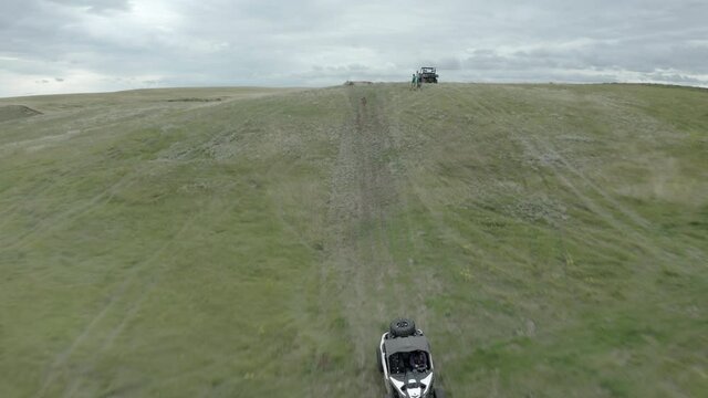 Exhilarating fast low flight of off-road buggy airborne on green dirt hillside road in flat countryside, Swift Current, Saskatchewan, Canada, rising aerial