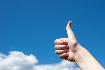 Gesture, thumb up on a background of blue sky and clouds, copy space. Motivation at work concept, business concept