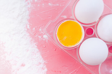 white eggs and one broken egg with yolk on a soft pink background with scattered flour, top view