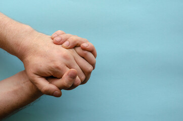 Interlocked fingers of two male hands on  blue background.
