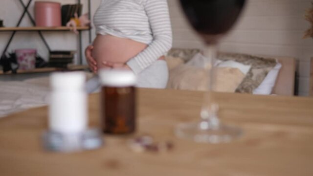 Close-up of a glass of red wine, pills and medicine on the table, a pregnant woman is sitting in the background. Refusal of alcohol and drugs during pregnancy.