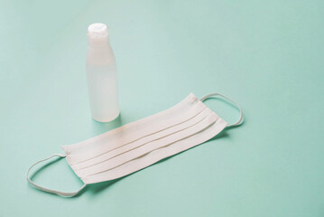 Sanitaser antiseptic gel bottle and protective facial mask on pastel azure background.