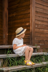 Little girl in a white boho dress and a hat against the background of a house.