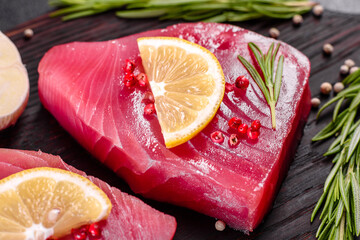 Fresh tuna fillet steaks with spices and herbs on a black background