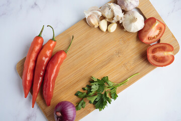 Wooden board with clear space. Around tomato, parsley, chili pepper, onion and garlic. Top views.