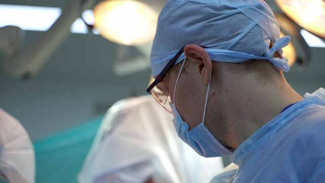 Profile view of a doctor. Face of a medical male specialist in blue uniform and glasses during the surgery in the operating room.