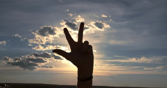 The silhouette of a female hand shows in the international sign language the phrase I love you against the backdrop of a sunset sky.