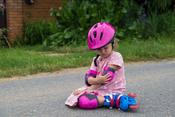 A little girl roller skating in full protection fell on the asphalt