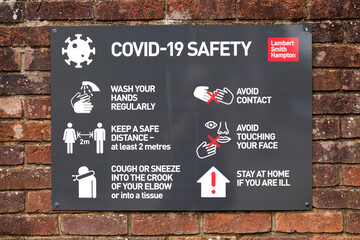 COVID 19 safety information sign for shoppers mounted on brick wall leading to town centre shopping area
