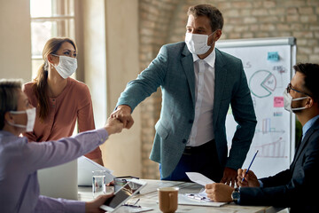 Happy colleagues with face masks fist bumping on a meeting in the office.