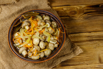 Delicious marinated mushrooms with carrot, onion and spices in ceramic bowl on wooden table. Top view