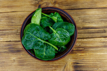 Fresh green spinach leaves in bowl on a wooden table. Top view