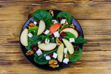 Autumn spinach salad with apple, feta cheese, walnut and dried cranberry on wooden table. Top view. Healthy vegetarian food
