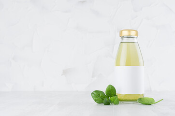 Fresh vegetable green spinach juice in glass bottle with blank label template with leaves on wood table and white background with copy space.